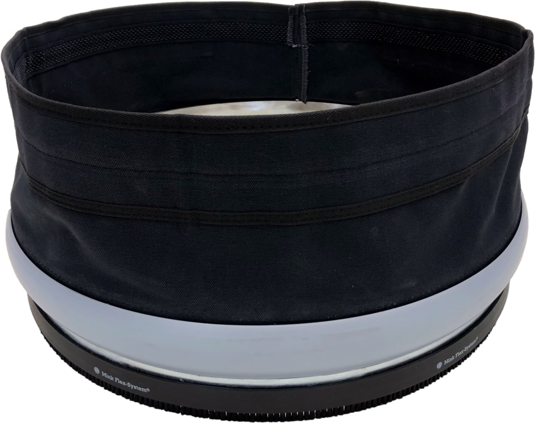 PALLMANN_dummy_SPIDER DUST SEALING SLEEVE_msl_2018-04 Крупный план верхней кромки и отверстия цилиндрического изделия из черной ткани или шляпы. На фото видна круглая внутренняя полость с черной подкладкой, видимыми усиленными швами и несколькими горизонтальными тканевыми лентами снаружи. Ближе к нижнему краю расположены два широких светло-серых пластиковых кольца и ребристая черная резиновая основа с мелкими зубчиками и частично видимой печатью «Mink Flex-System®». Ткань имеет грубую структуру плетения и матовую поверхность; изделие смотрится упругим, но гибким. Освещение ровное, фон белый.